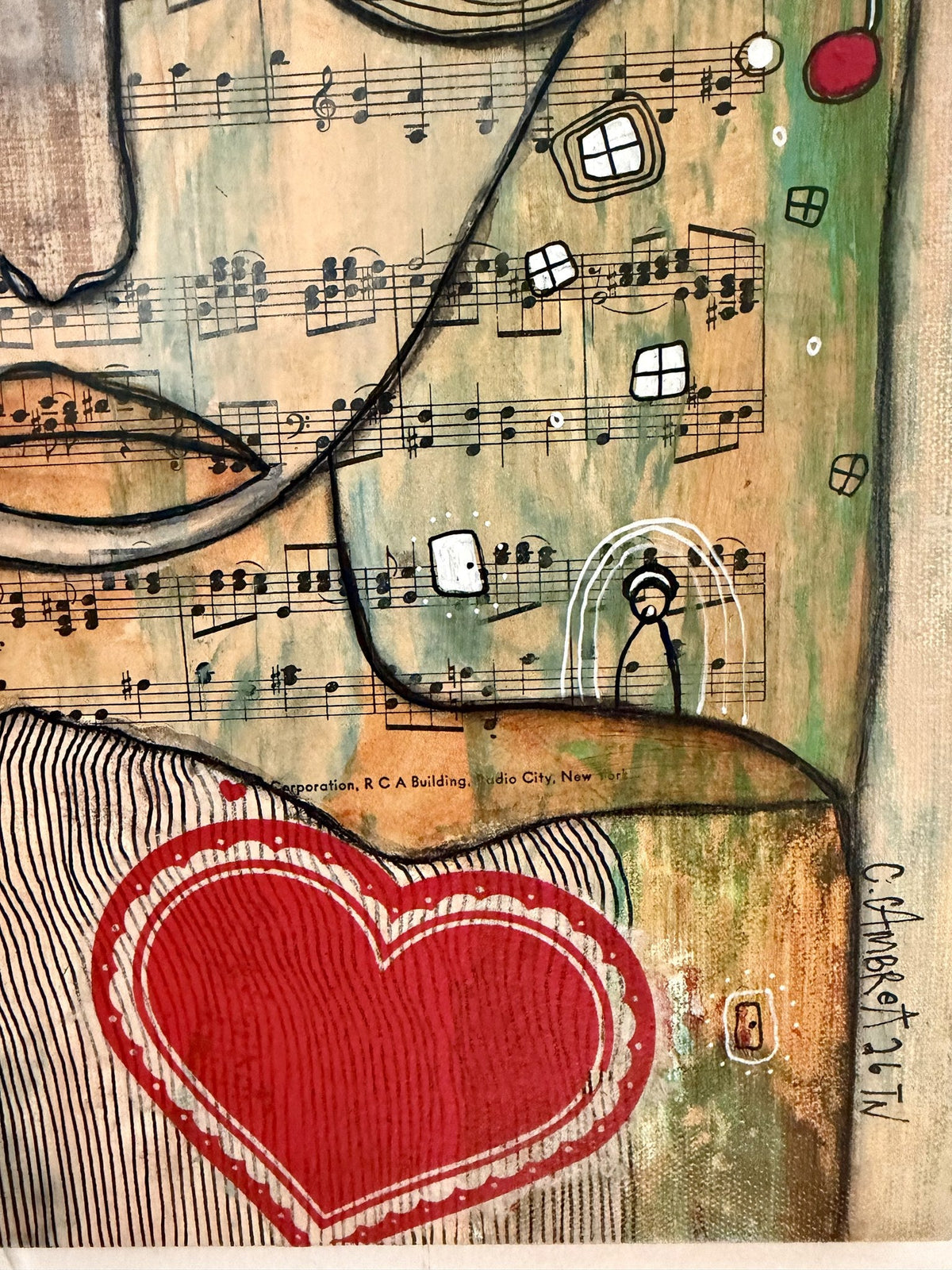 Detail of a red heart on striped fabric with sheet music background and the artist's signature.