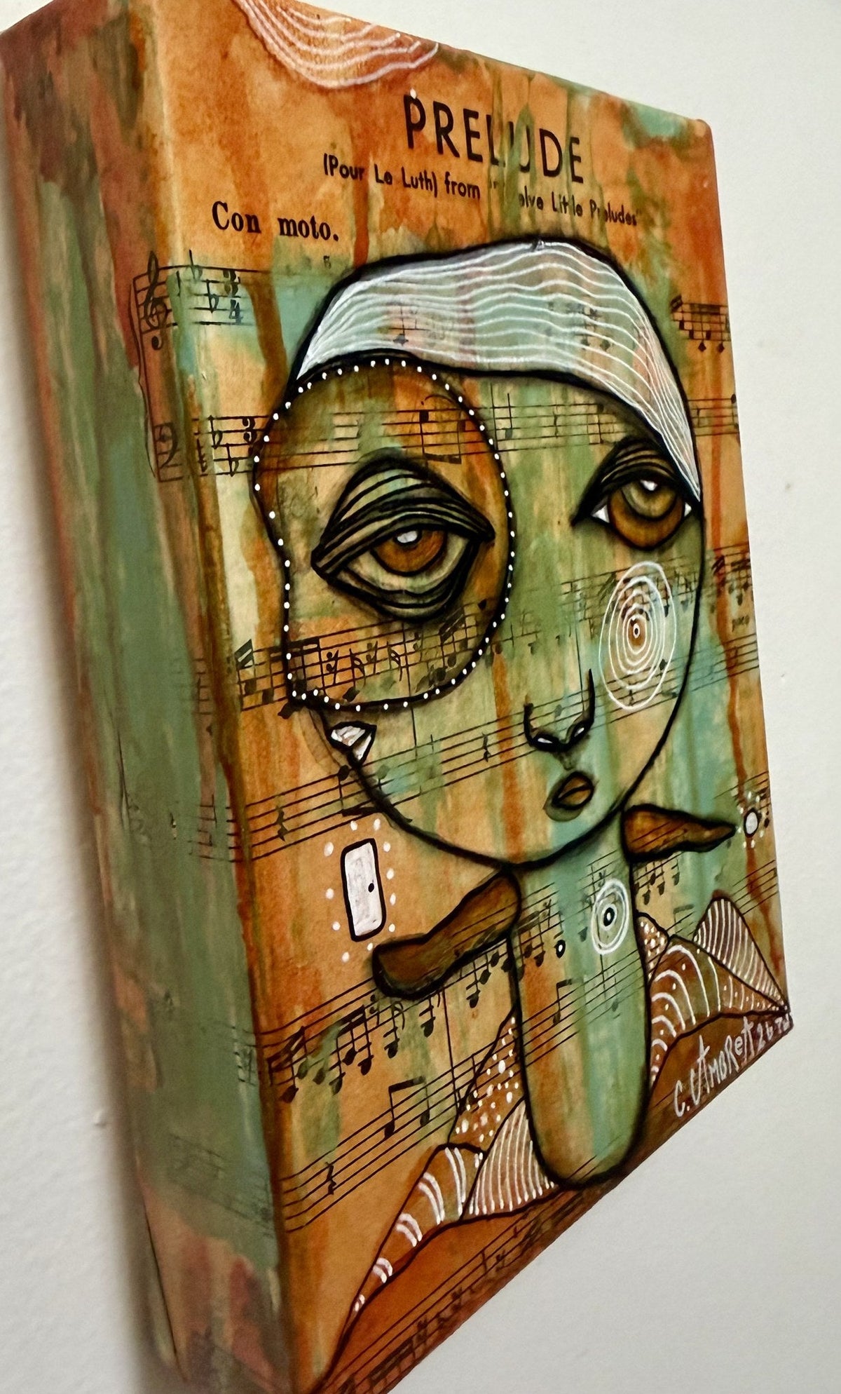 Closer angled view of mixed media canvas artwork, revealing dimensional texture and hidden faces within patterns