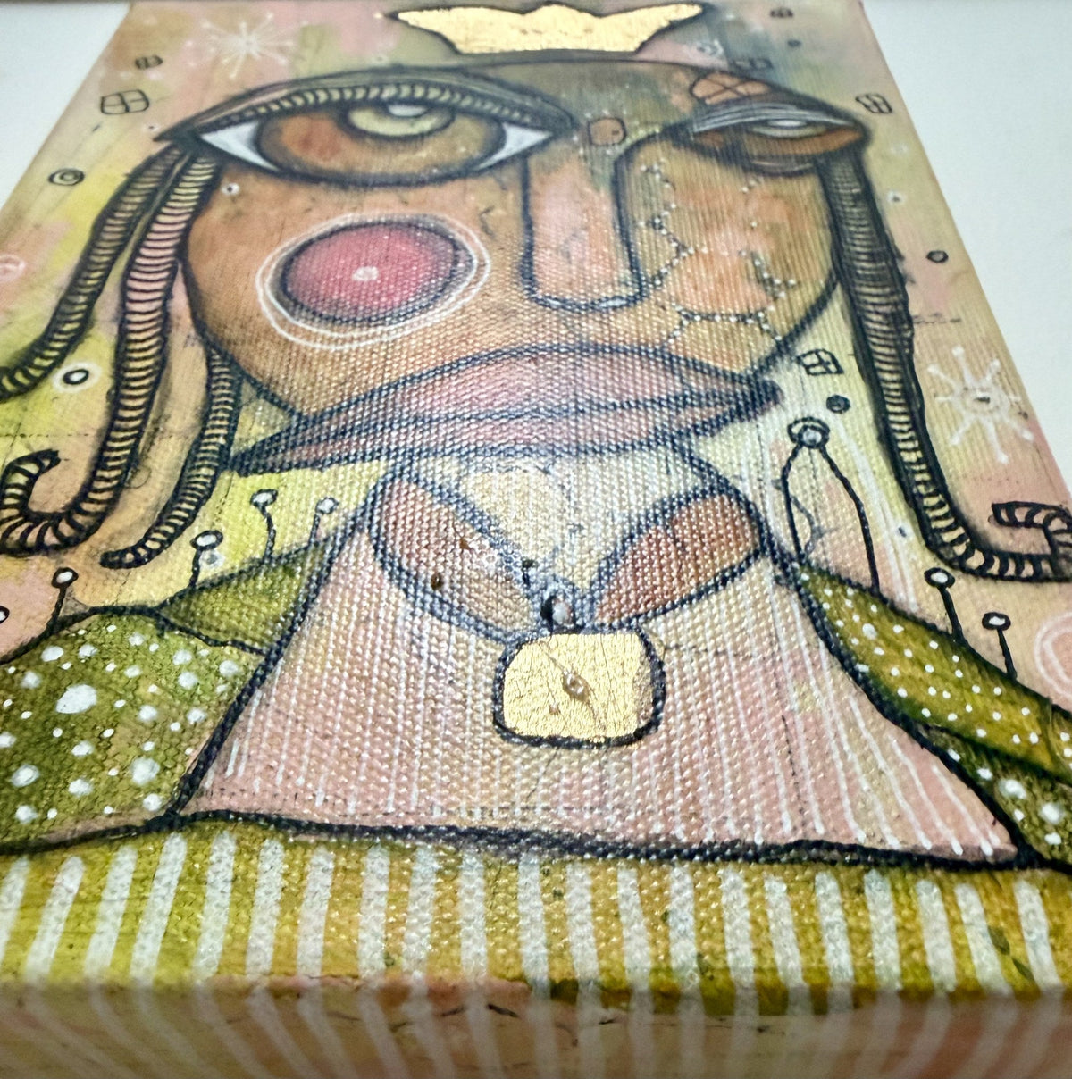 Angled close-up highlighting the painting's textured canvas weave, gold leaf crown, and delicate linework.
