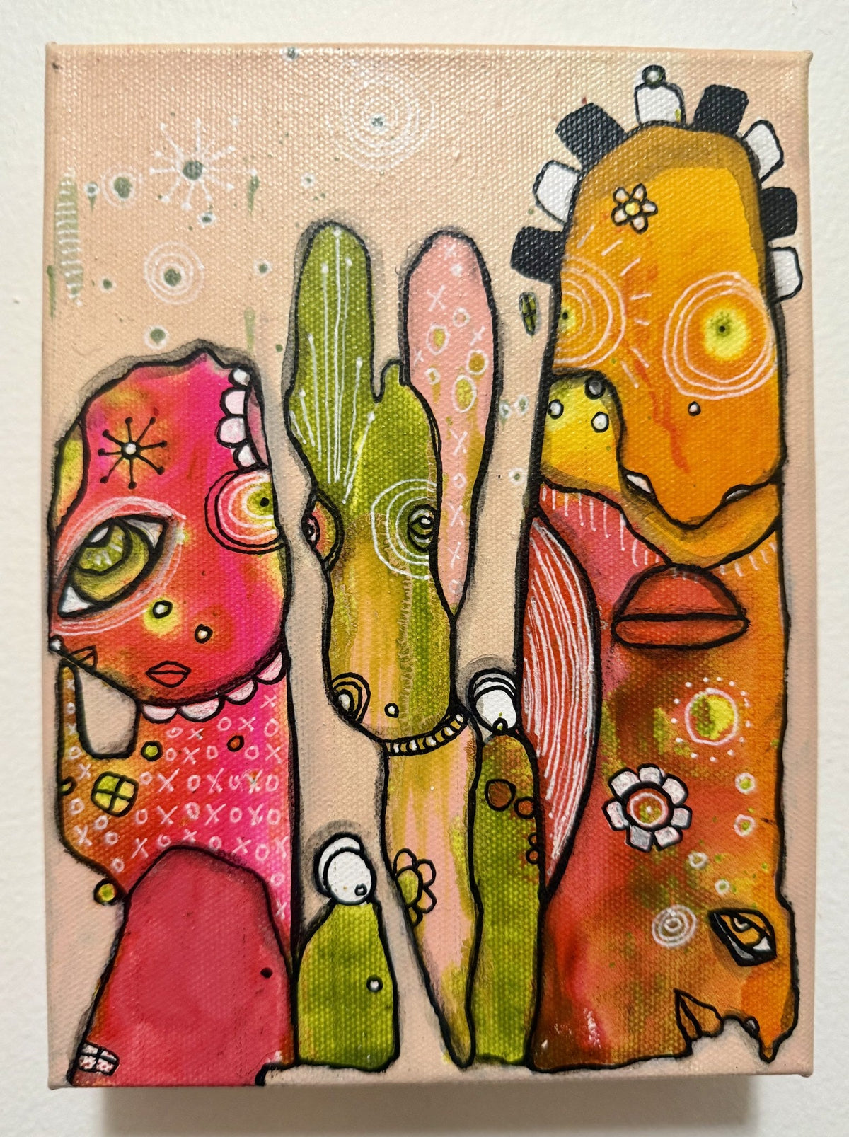 Full view of a mixed media canvas painting with three whimsical pareidolia faces in pink, green, and orange.