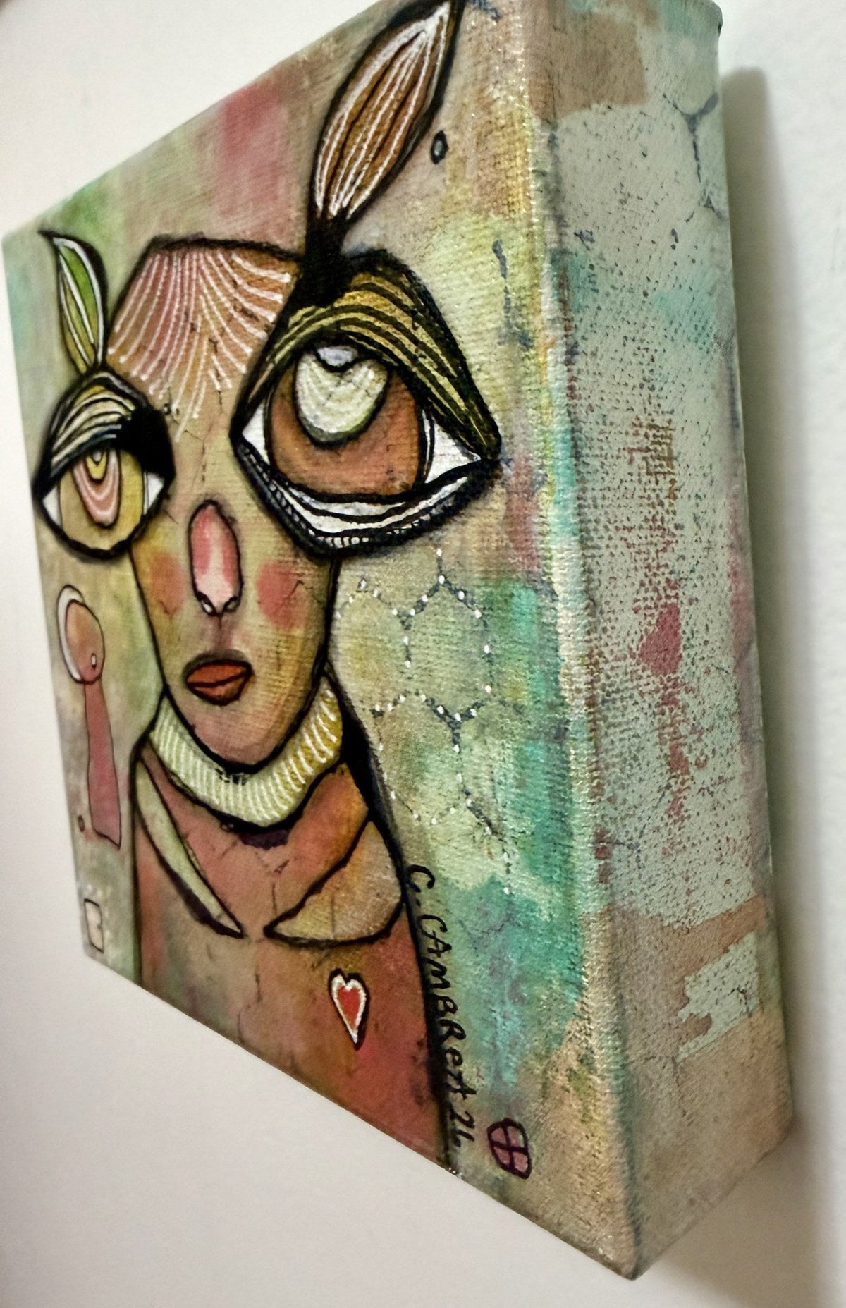 Angled detail view showing the canvas depth, textured eyes, honeycomb pattern, and a small pink figure hidden beside the face.