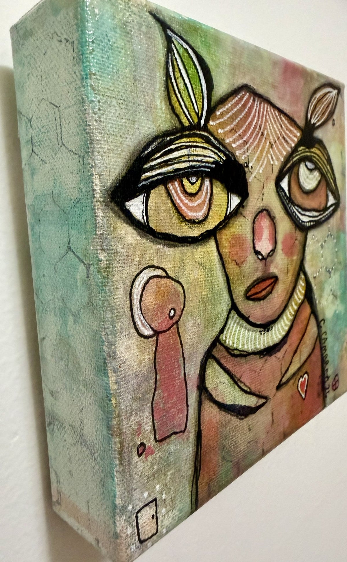 Side-angle detail view of the painted face and rabbit-ear lashes against a shimmering green and pink hexagon-patterned background.